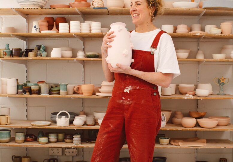 Brittney Kleyn smiling and holding a large pink vase in front of shelves of ceramics